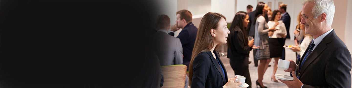 A group of business professionals is seen networking and conversing in a modern indoor setting.