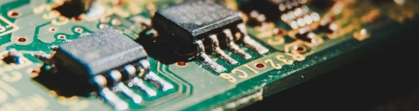 A detailed view of a green circuit board featuring multiple black microchips and intricate wiring. 
