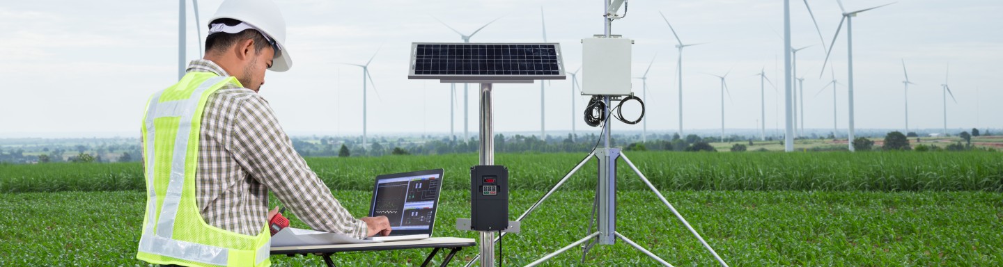 Técnico en laptop frente a turbinas eólicas tomando mediciones