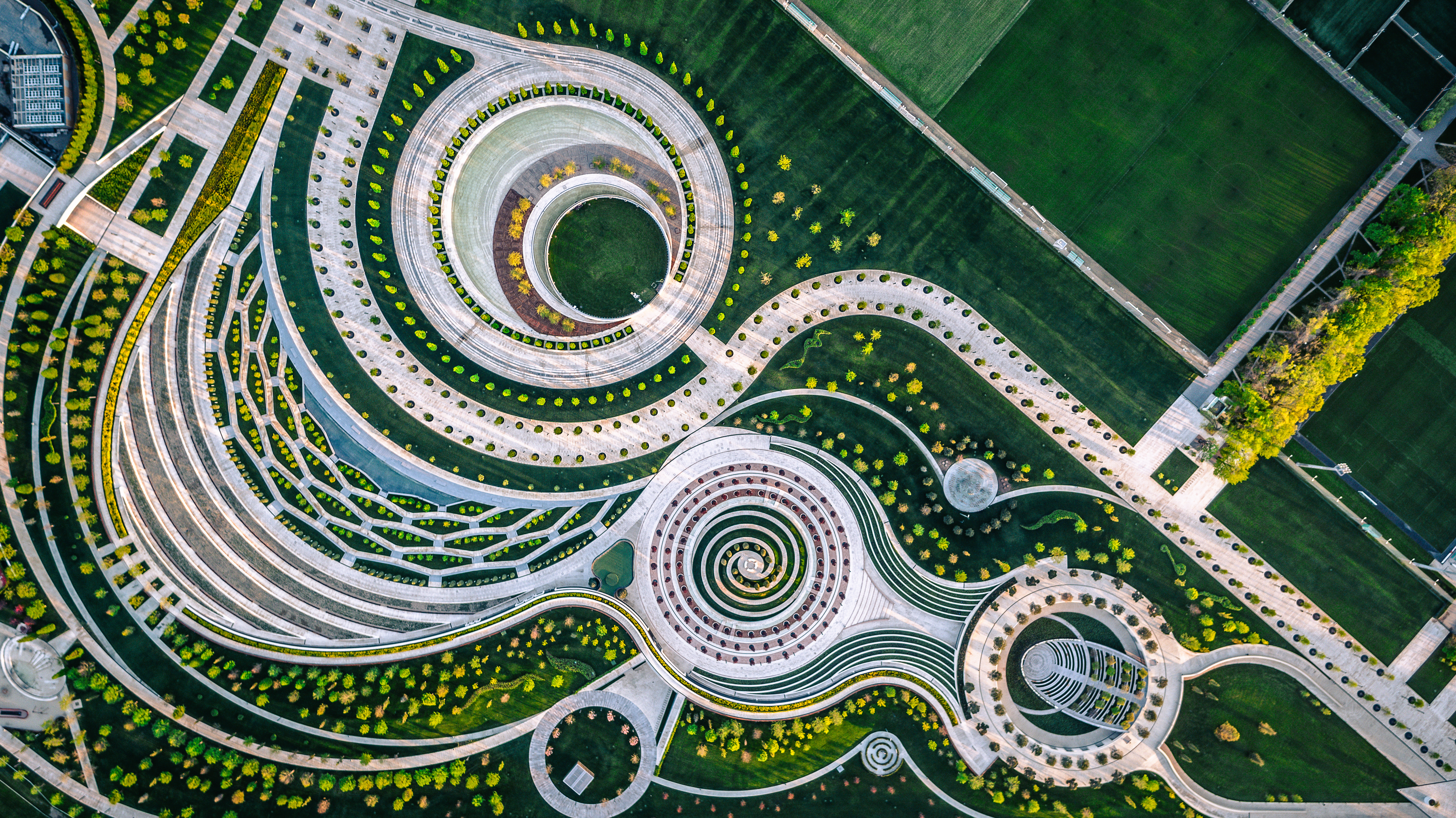 Aerial view of a large, artistically designed garden featuring concentric circles, spirals, and geometric patterns with pathways, green lawns, and planted areas