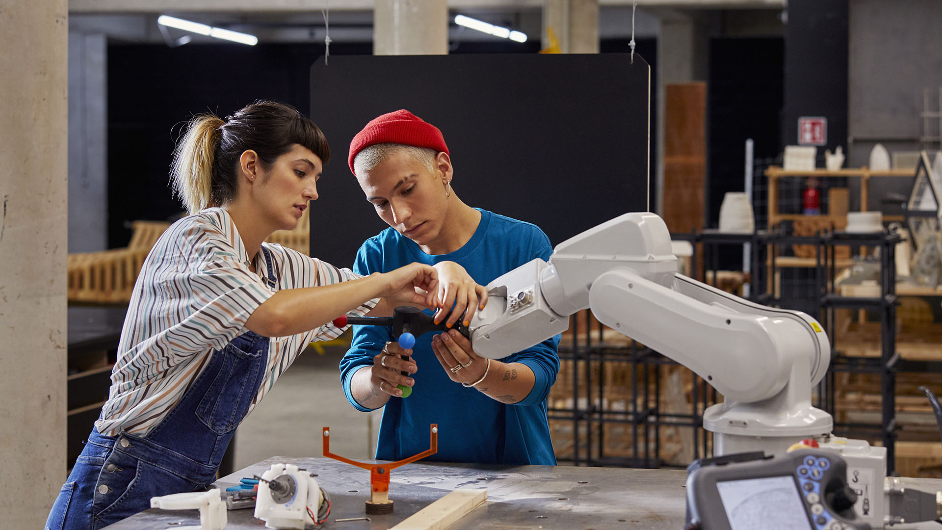 Two individuals work together with a robotic arm in an industrial setting. 