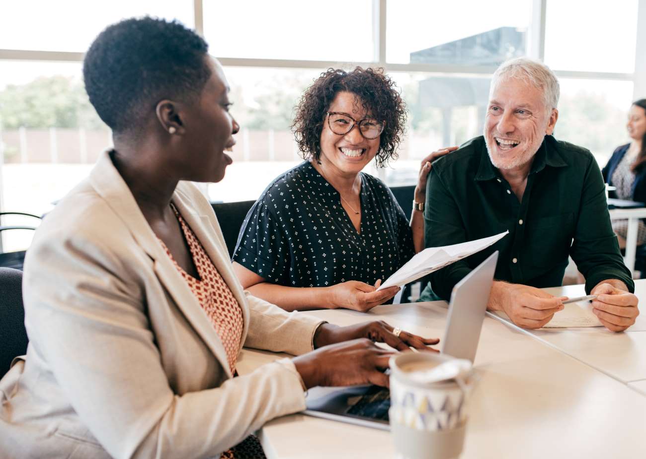 Mixed_Gender_Meeting Three People Sitting At A Table In Conversation Smiling