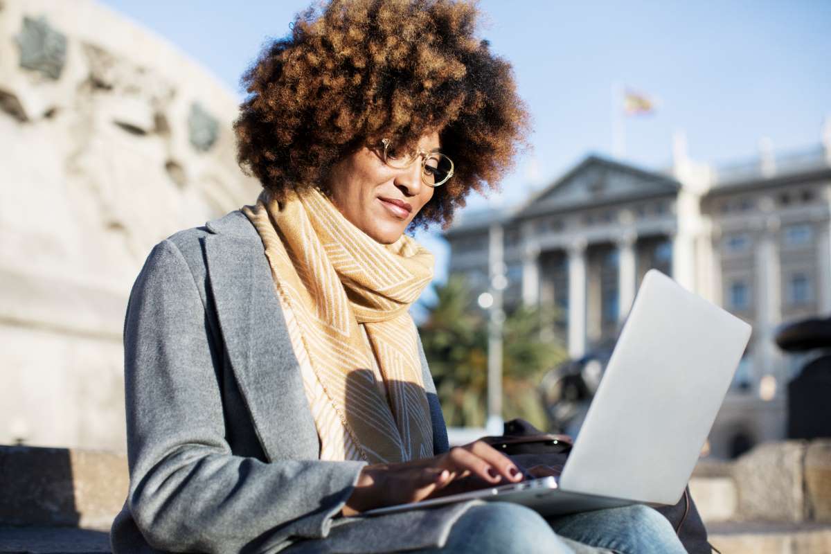 Woman using laptop while sitting on steps in a city